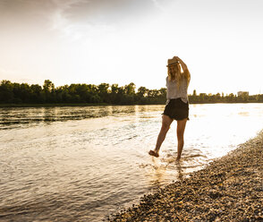 Junge Frau läuft abends barfuß am Flussufer - UUF14037