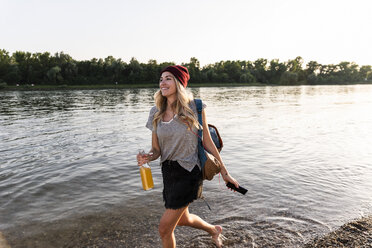 Junge Frau läuft barfuß am Flussufer, Kopfhörer und Smartphone - UUF14042