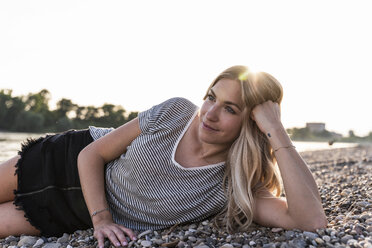 Young blond woman lying at riverside against evening sun - UUF14048