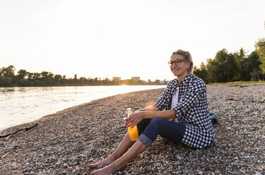 Blond woman sitting on riverside in the evening - UUF14058