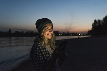 Junge Frau benutzt ihr Smartphone abends am Flussufer - UUF14073