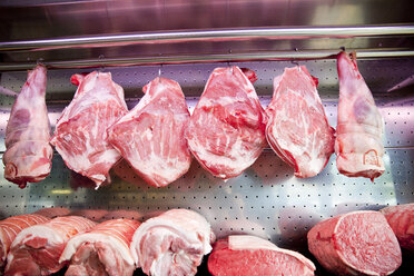 Rows of meat joints hanging in refrigerator at butchers shop - CUF23597
