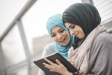 Zwei junge Frauen mit Hidschab, die auf einer Fußgängerbrücke ein digitales Tablet benutzen - CUF23611