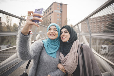 Zwei Freundinnen auf einer Fußgängerbrücke machen ein Smartphone-Selfie - CUF23612