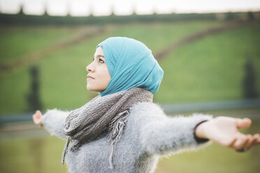 Junge Frau im Park mit geöffneten Armen und türkisfarbenem Hijab - CUF23630