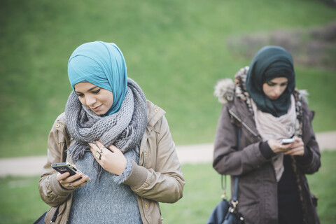 Zwei Freundinnen im Park lesen Texte auf Smartphones, lizenzfreies Stockfoto