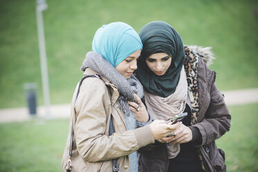 Zwei Freundinnen im Park lesen Texte auf ihren Smartphones - CUF23632