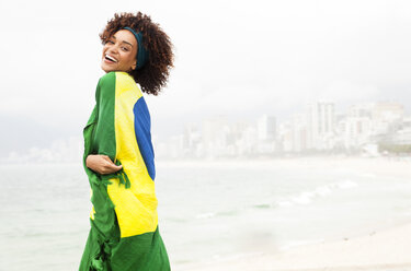 Porträt einer jungen Frau, eingewickelt in die brasilianische Flagge am Strand von Ipanema, Rio De Janeiro, Brasilien - CUF23656