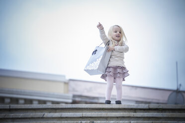 Young girl pointing from stairway carrying shopping bag, Cagliari, Sardinia, Italy - CUF23705
