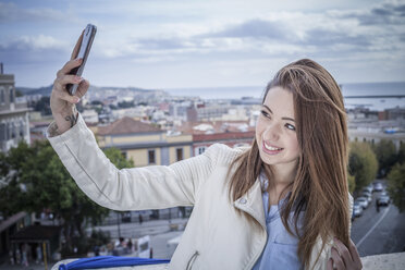 Young woman on rooftop taking smartphone selfie, Cagliari, Sardinia, Italy - CUF23711