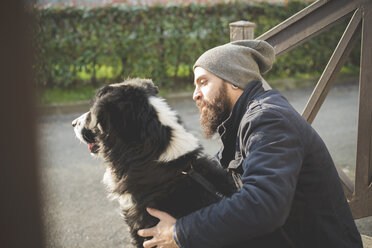 Mittlerer erwachsener Mann mit Hund sitzend, im Freien - CUF23723