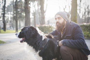 Mid adult man, crouching, stroking dog, outdoors - CUF23724