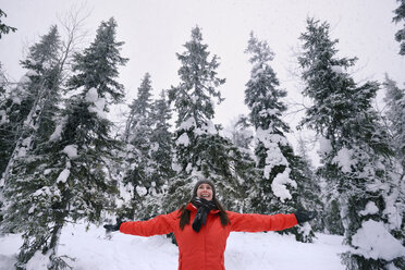 Young woman celebrating in snow covered forest, Posio, Lapland, Finland - CUF23735