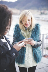 Two young women texting on smartphones at Lake Como, Como, Italy - CUF23741