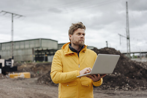 Mann hält Laptop, Baustelle im Hintergrund - KNSF03977