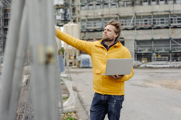 Man holding laptop, construction site in the background - KNSF03980