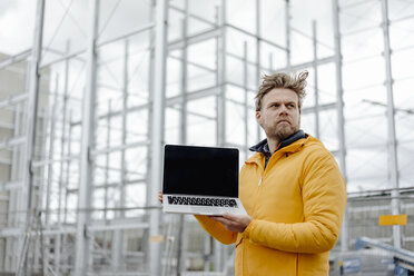 Man holding laptop, construction site in the background - KNSF03982