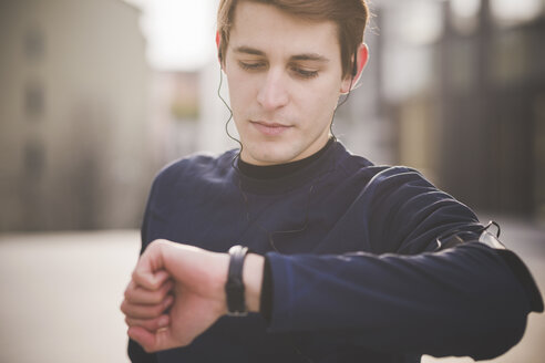 Junger männlicher Läufer, der auf dem Stadtplatz seine Armbanduhr überprüft - CUF23767