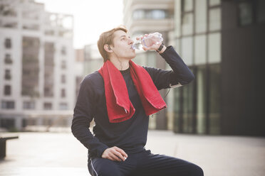 Young male runner drinking water on bench in city square - CUF23770