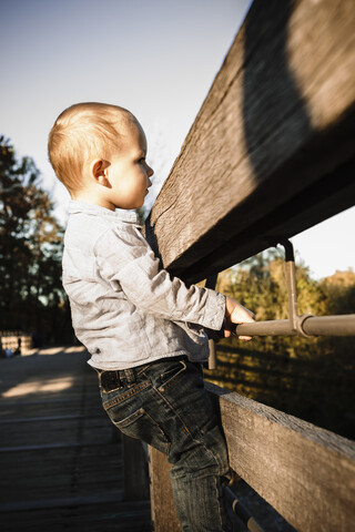 Kleiner Junge hält sich an einem Holztor in ländlicher Umgebung fest, lizenzfreies Stockfoto