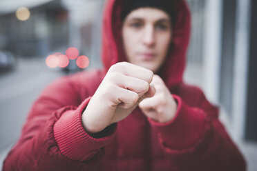 Nahaufnahme eines jungen Mannes, der mit geballten Fäusten auf einer Straße in der Stadt posiert - CUF23825