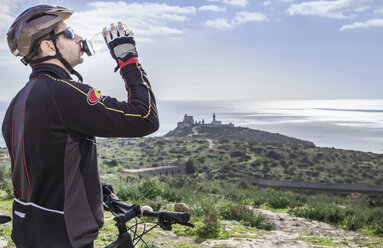 Mittlerer erwachsener männlicher Mountainbiker trinkt Wasser auf einem Küstenweg, Cagliari, Sardinien, Italien - CUF24038