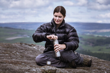 Junge Wanderin beim Öffnen einer Flasche auf der Spitze von Guise Cliff, Pateley Bridge, Nidderdale, Yorkshire Dales - CUF24046