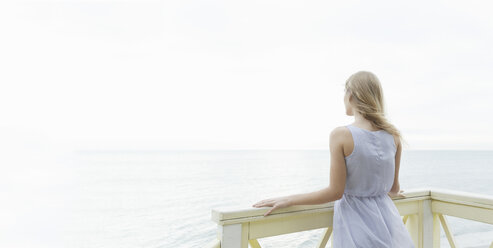Rear view of young woman looking out to sea from balcony, Miami Beach, Florida, USA - CUF24060