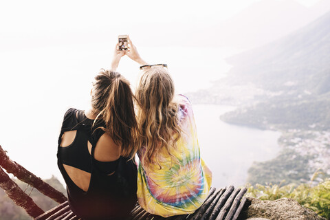 Rückansicht von zwei Freundinnen, die ein Smartphone-Selfie am Atitlan-See, Guatemala, machen, lizenzfreies Stockfoto