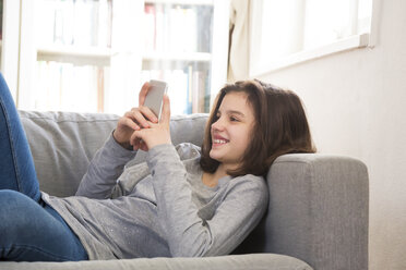 Smiling girl lying on couch at home using cell phone - LVF07046