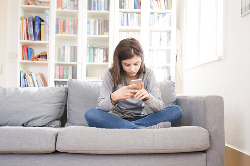 Mädchen sitzt zu Hause auf der Couch und benutzt ein Mobiltelefon - LVF07048