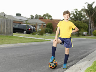 Portrait of boy with foot on soccer ball on suburban road - CUF24110