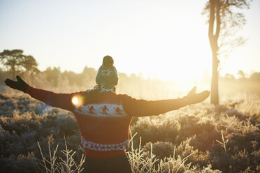 Rückansicht eines Mannes in Winterkleidung mit offenen Armen im Sonnenlicht - CUF24113