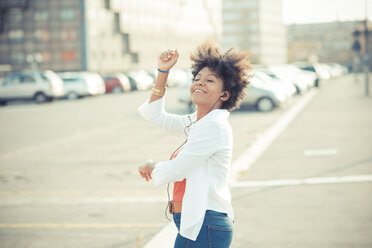 Junge Frau tanzt zu Musik mit Kopfhörern in der Stadt - CUF24144