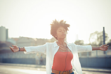 Young woman dancing with arms open to smartphone music in city - CUF24145