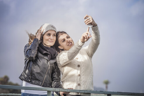 Zwei junge Freundinnen benutzen den Touchscreen für ein Smartphone-Selfie an der Küste - CUF24161