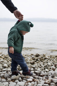 Kleines Mädchen an der Hand des Vaters, das auf den Kieselsteinen am Seeufer steht, Starnberger See, Bayern, Deutschland - CUF24175
