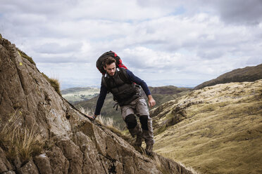 Junger männlicher Wanderer, der von einem Felsen herabsteigt, The Lake District, Cumbria, UK - CUF24178