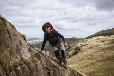 Young male hiker stepping from rock, The Lake District, Cumbria, UK - CUF24178