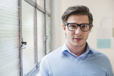 Portrait of young businessman next to office window - CUF24254