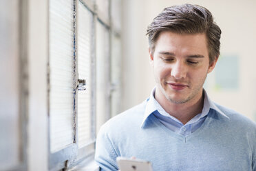 Junger Geschäftsmann, der im Büro eine SMS auf seinem Smartphone schreibt - CUF24256