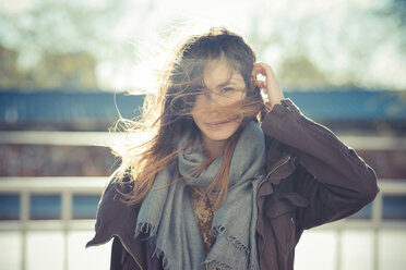 Mid adult woman standing on breezy roadside with hand in hair - CUF24268