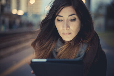 Mittlere erwachsene Frau, die auf einem Bahnsteig in der Abenddämmerung den Touchscreen eines digitalen Tablets benutzt - CUF24275