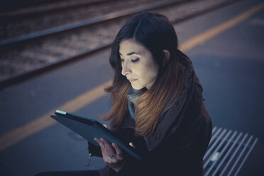 Mid adult woman using digital tablet on railway platform at dusk - CUF24276