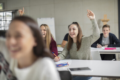 Glückliche Mädchen im Teenageralter, die im Unterricht die Hände heben, lizenzfreies Stockfoto