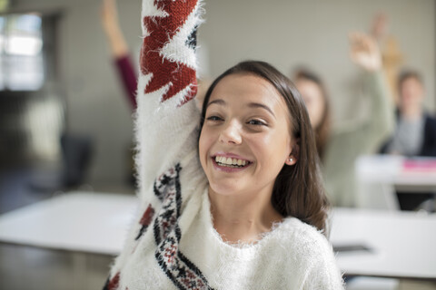 Smiling teenage girl raising hand in class stock photo