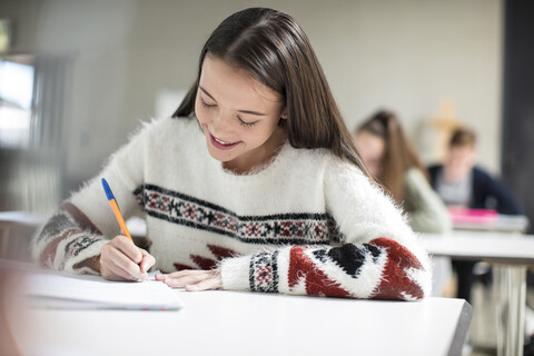 Lächelndes Teenager-Mädchen, das in der Klasse in ein Schulheft schreibt, lizenzfreies Stockfoto