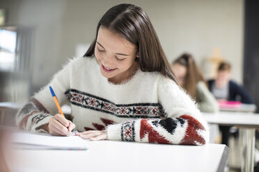 Lächelndes Teenager-Mädchen, das in der Klasse in ein Schulheft schreibt - ZEF15658