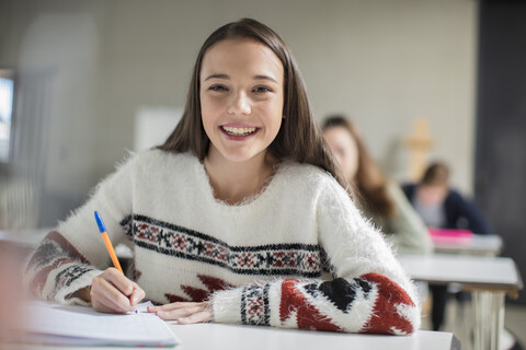 Porträt eines lächelnden Teenagers, der im Unterricht in ein Schulheft schreibt, lizenzfreies Stockfoto
