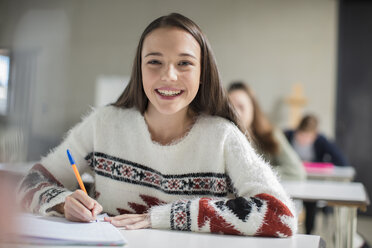 Portrait of smiling teenage girl writing in exercise book in class - ZEF15659